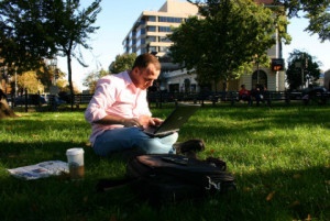 alternatives to working at your desk: a man sitting on grass with a laptop used in blog 10 unique alternatives to working at your desk