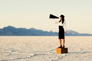 A woman stands on a box in the desert speaking into a horn, used for blog 'How to get employees invested in your business goals'